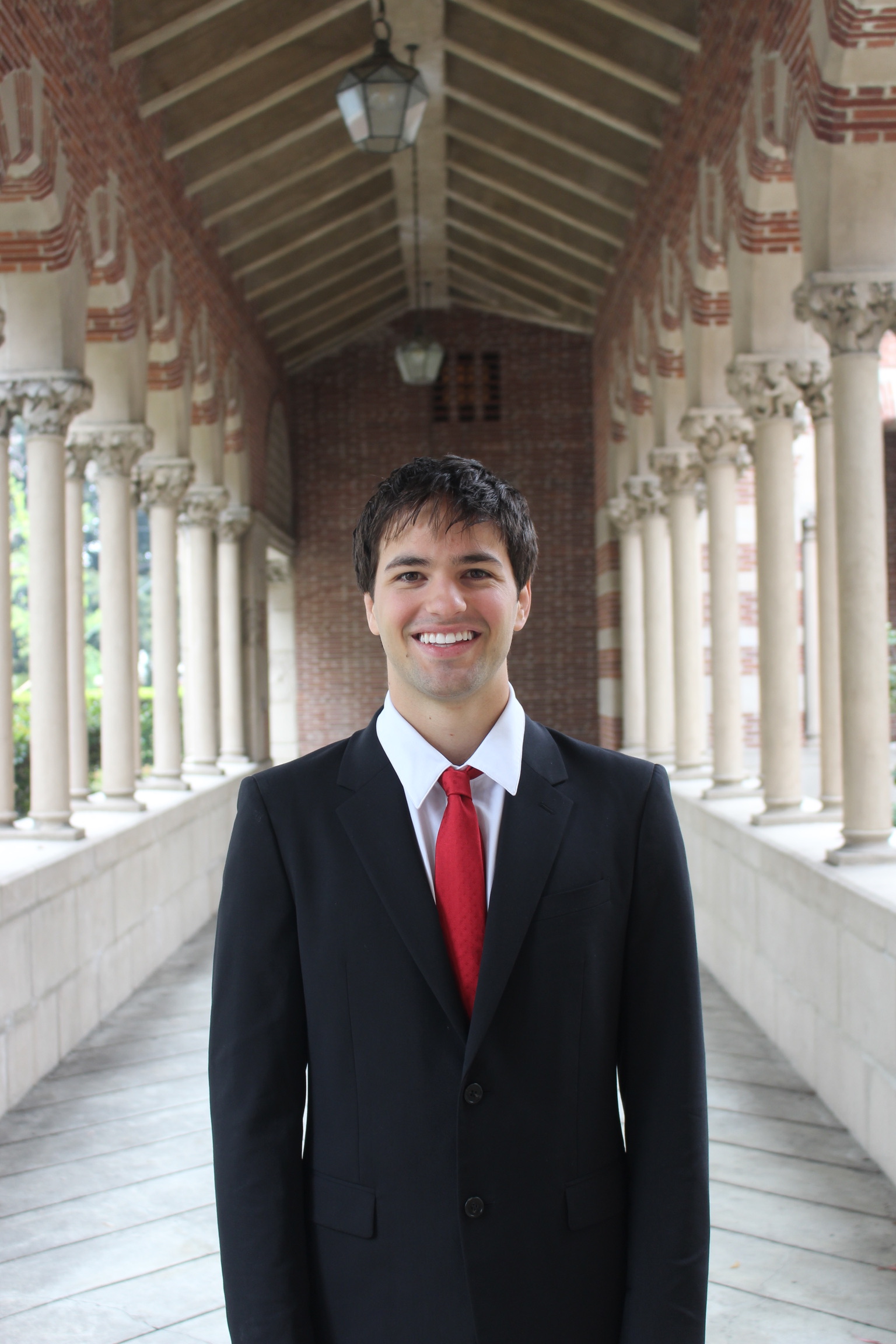 Portrait of Tyler Davis in a suit and red tie beneath a campus colonnade