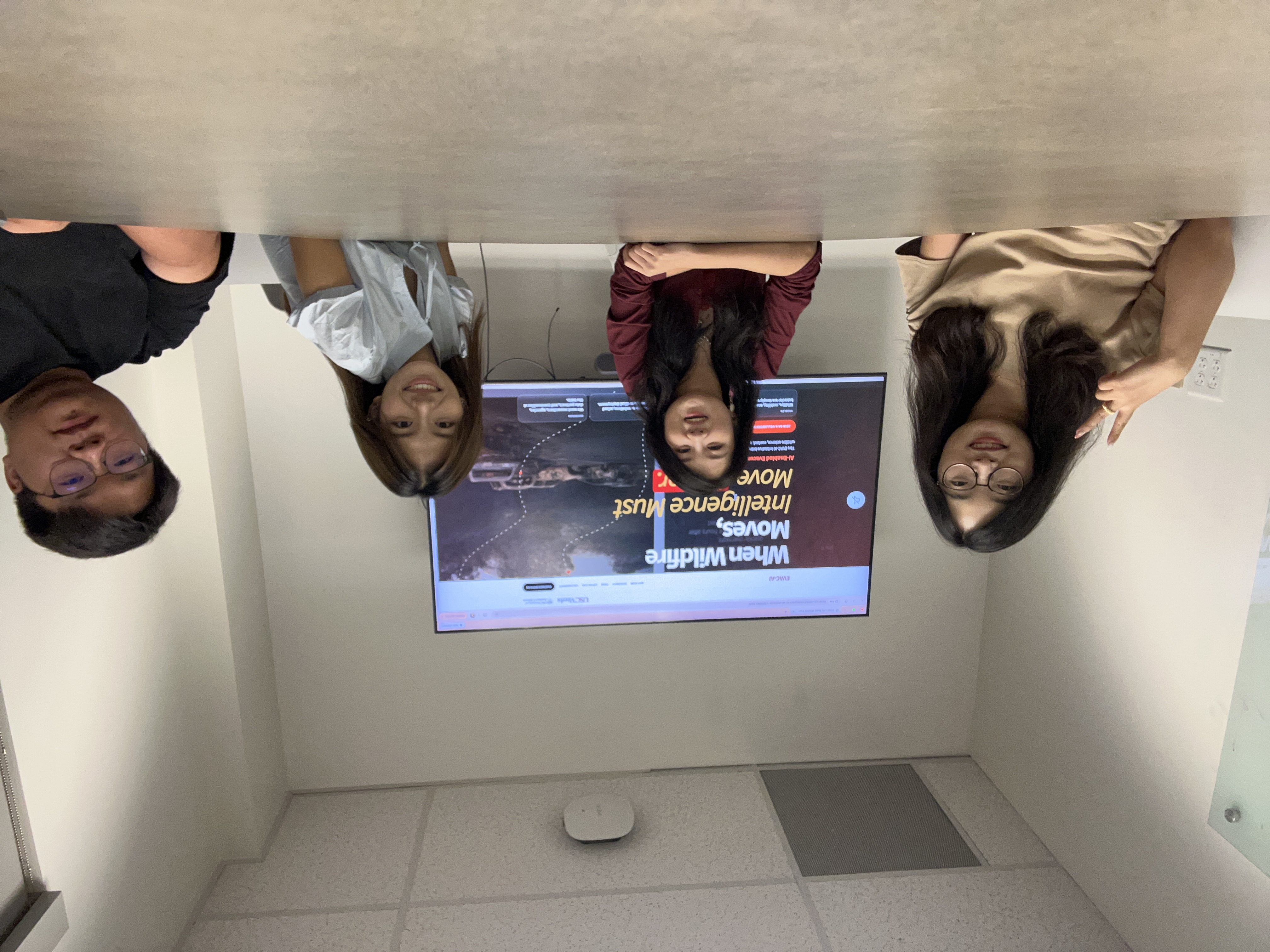 Four team members gathered around a table with the EVAC-AI website on a screen behind them.